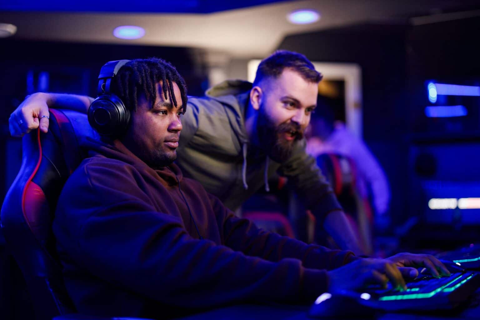 Multicultural gamer is playing video game while is friend is cheering