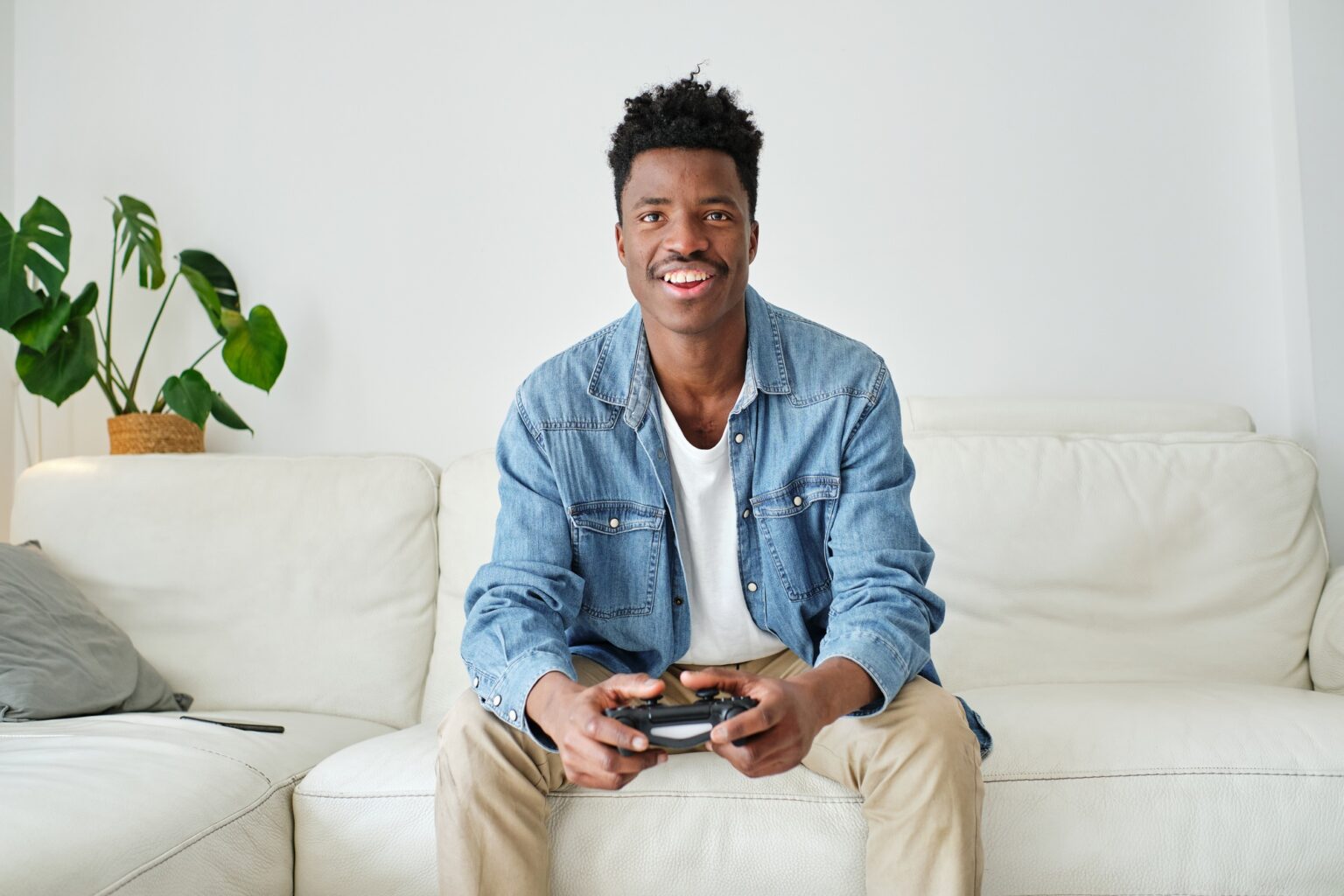 7 jeux vidéo incontournables pour débuter sur PS4 et PS5 Happy black man with game pad playing on sofa