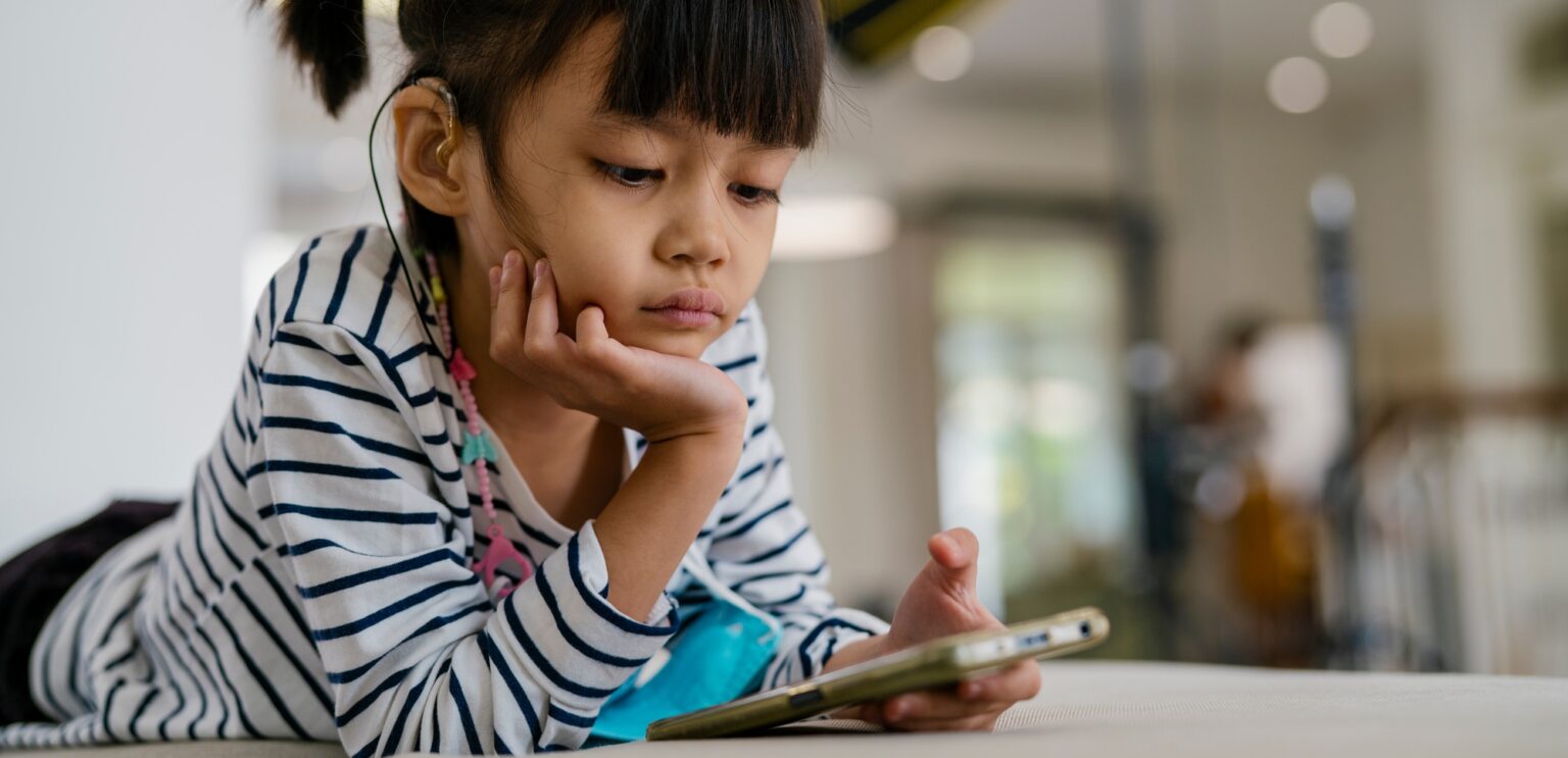 School Time : la fonctionnalité intégrée à son application de contrôle parental de Google Asian girl wearing a hearing aid and playing a smartphone.