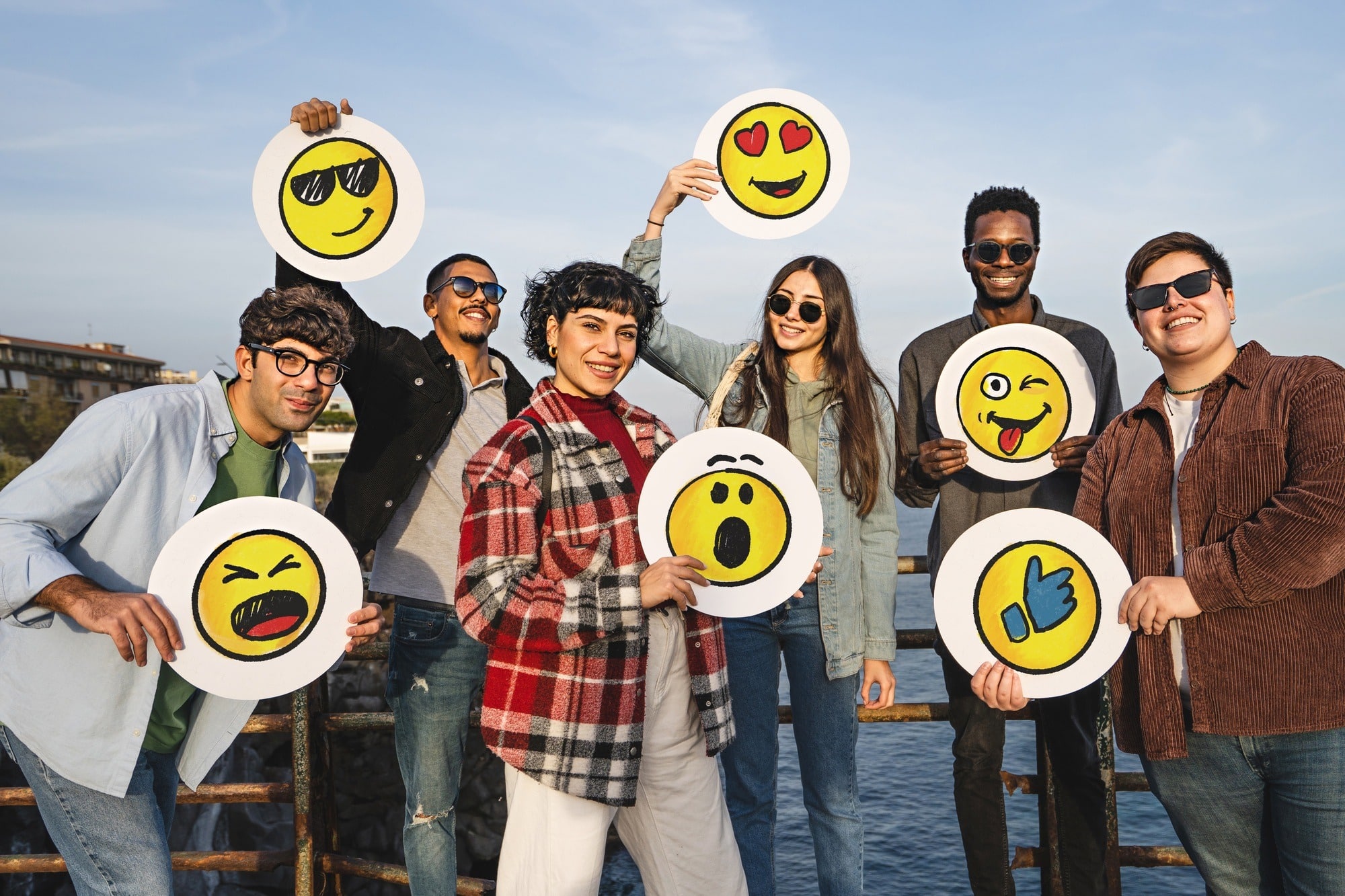Group of happy positive friends holding discs with handdrawn emoji smiley faces standing outdoor