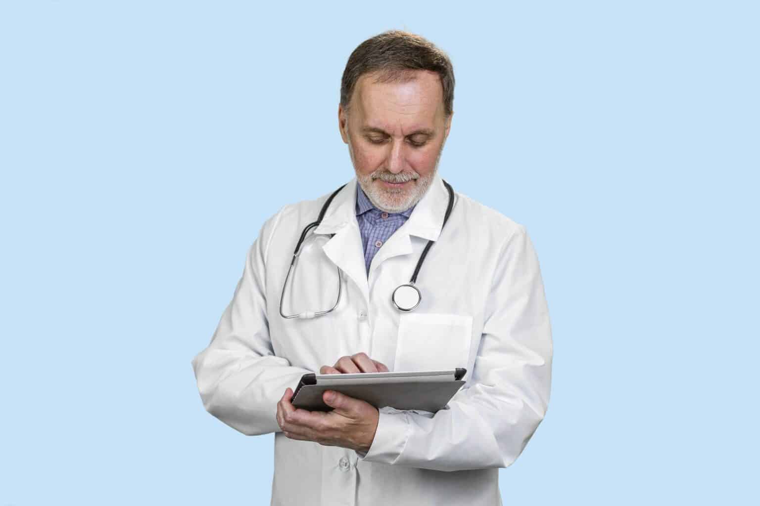 Old senior male doctor holding digital tablet in hands using health technology.