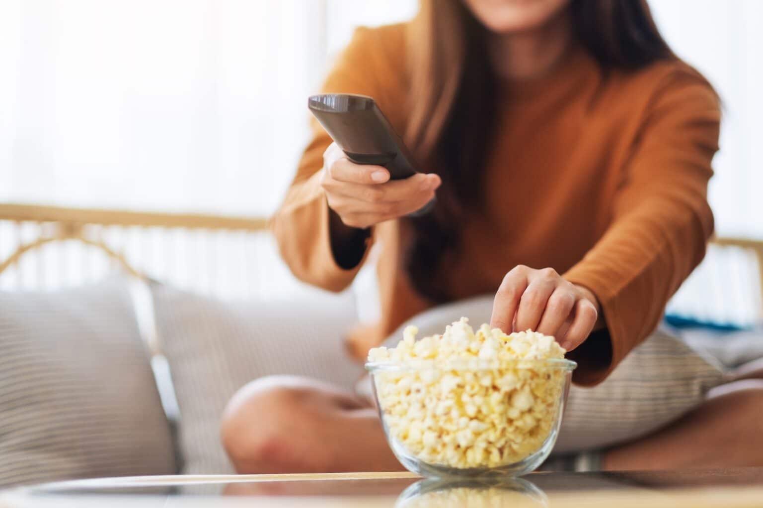 a young woman eating popcorn and searching channel with remote control to watch tv