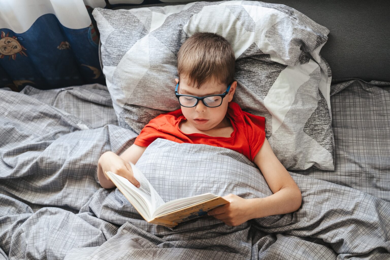 Différences entre Game of Thrones et les romans : ce que les viewers ne savent pas boy with glasses lies on a bed under a blanket and reads a book .child is reading a book in bed.